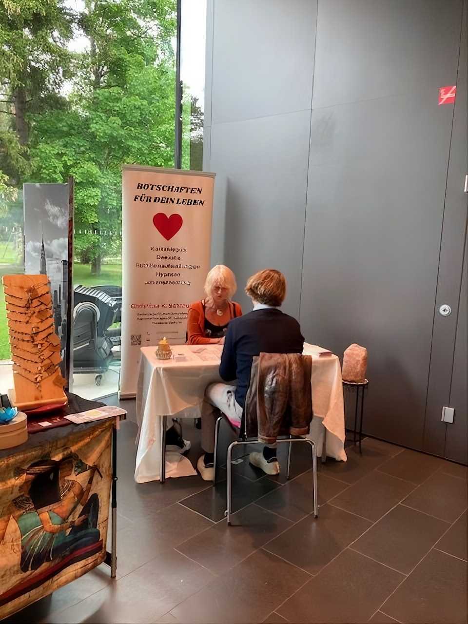 Beratungsgespräch am Infotisch neben Banner, ruhige Atmosphäre im Innenbereich.