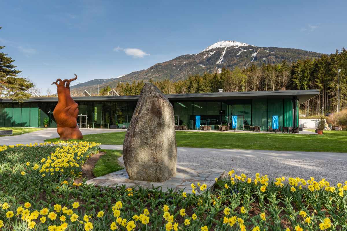 Congresspark Igls: Blick auf das Gebäude mit Skulptur, Stein und Blumenbeet im Vordergrund.