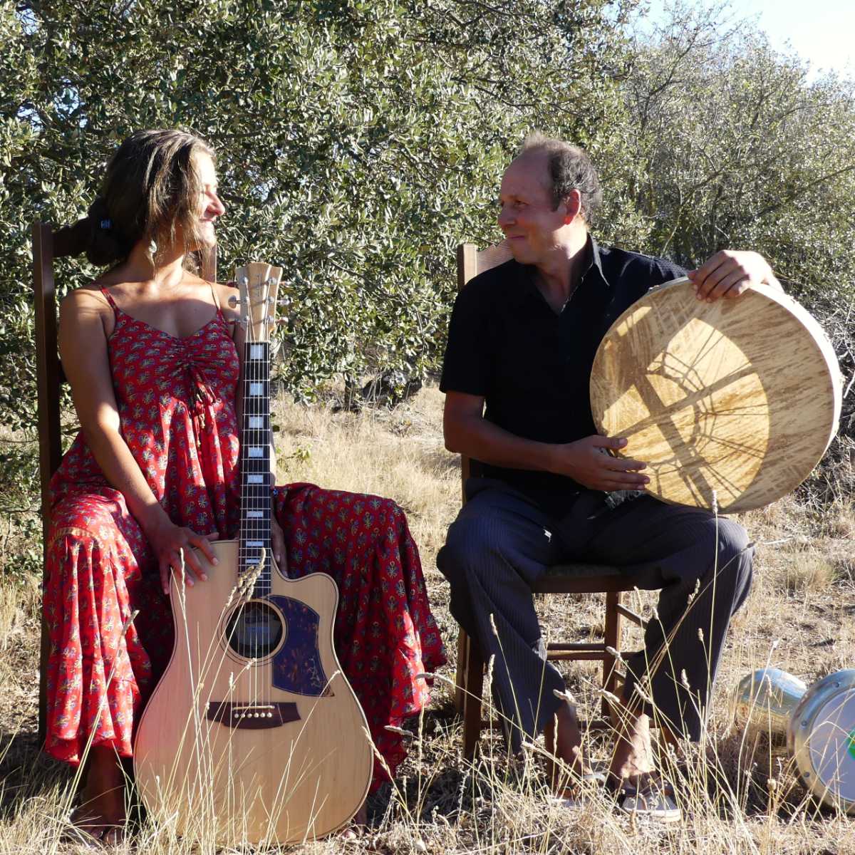 Luna y Sol sitzen im Freien mit Gitarre und Rahmentrommel einander gegenüber