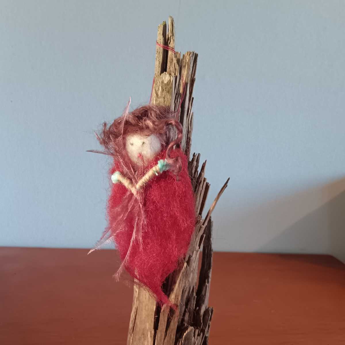 Handgefertigte kleine Figur aus roter Wolle und Naturholz auf einem Holztisch